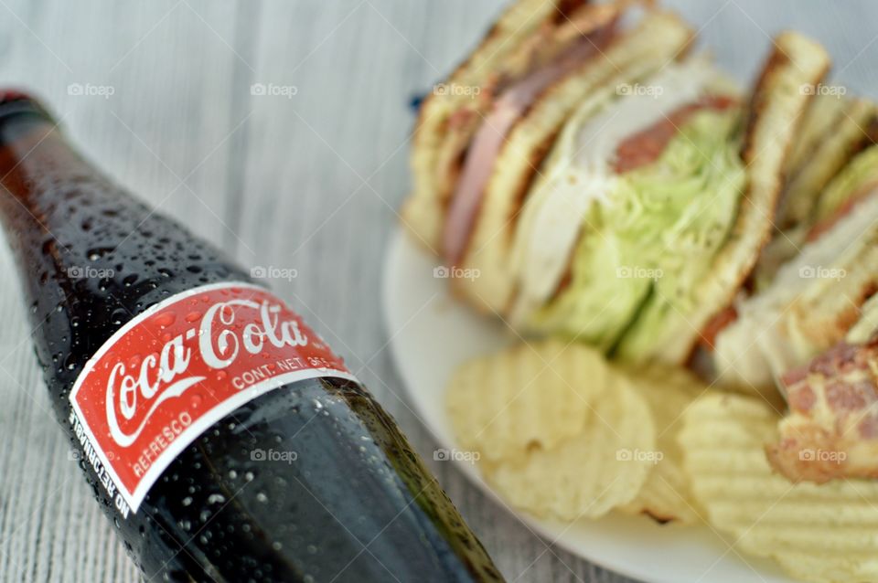 A can and a Bottle of Coca Cola with a club sandwich on a white rustic background 