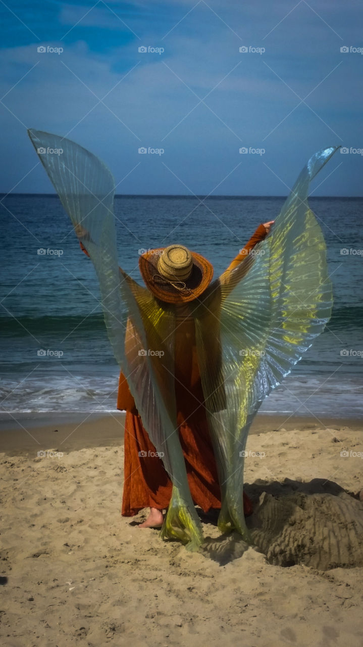 A beach reveler with Isis Wings worshipping the sun and waves in Monterey.