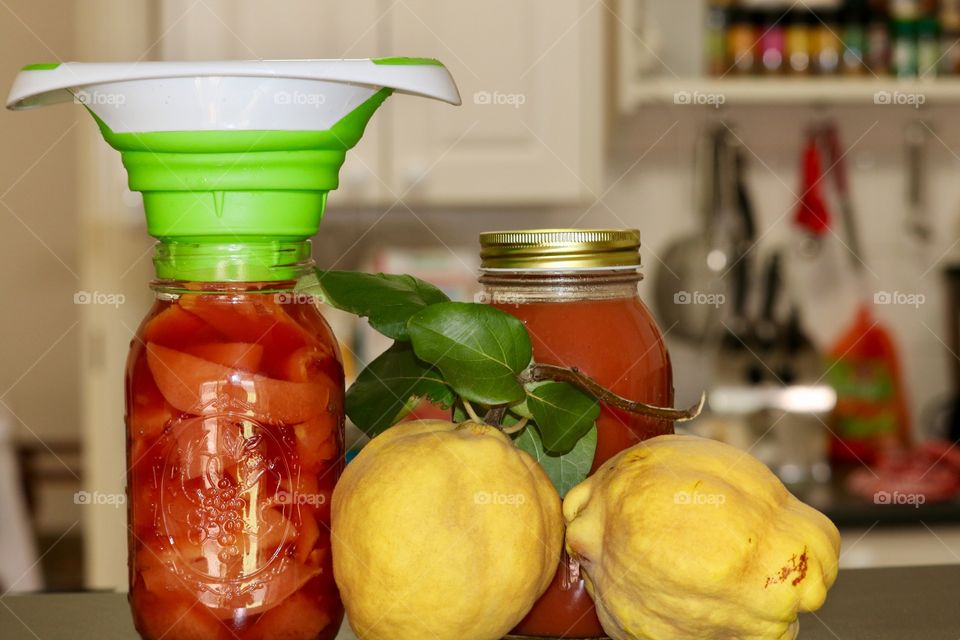 Fresh organic quince fruit prepared for canning, filling a canning jar with fresh preserves. Two jars foreground with funnel and blurred kitchen background 