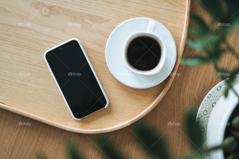 Top view of smartphone screen and cup of coffee through green houseplant