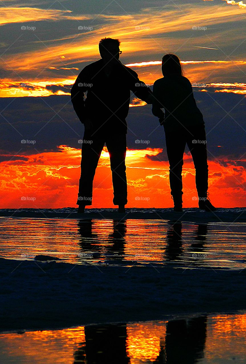 A loving couple show affection to each other during a stroll on the beach during a colorful sunset