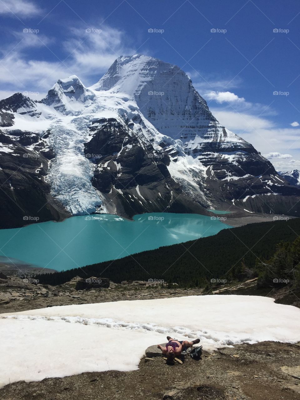 Exhausted hiker resting in the snow overlooking beautiful Berg Lake and Mount Robson Glacier in British Columbia Canada