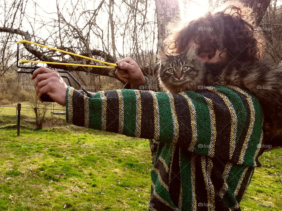 Hunky man shooting a slingshot with his cat.