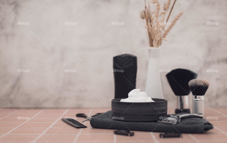 Wooden shaving foam bowl,terry towel,natural pile shaving brushes,combs,scissors,bottle of aftershave cream,razor,razor tips and yours with a dry shave stand right on stone brick background with copy space left,side view. Concept barbershop men,shavi