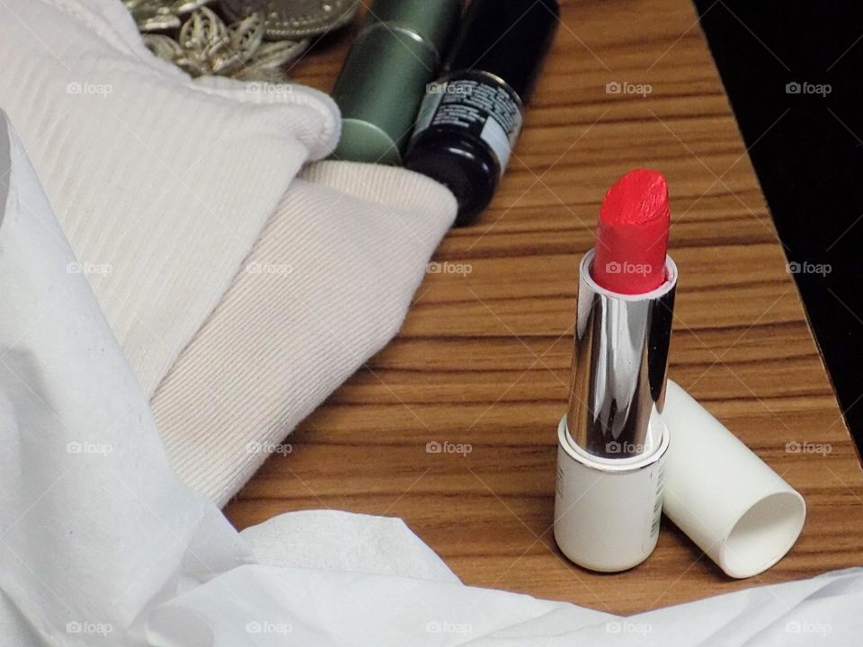 Lipstick, cloth and some women jewelery accessories on brown wooden table