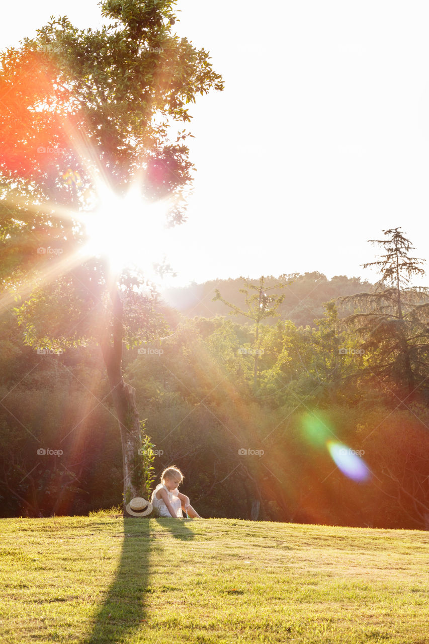 Kid sitting under tree on sunny day