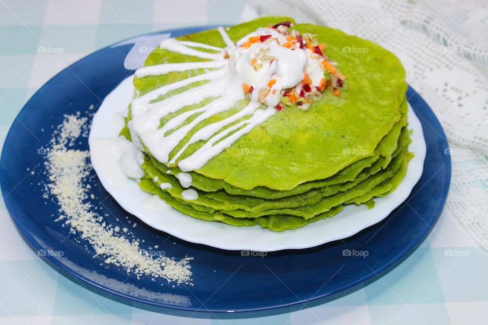 Spinach pancakes with sour cream and vegetables on a white and blue plate . Angle view of food