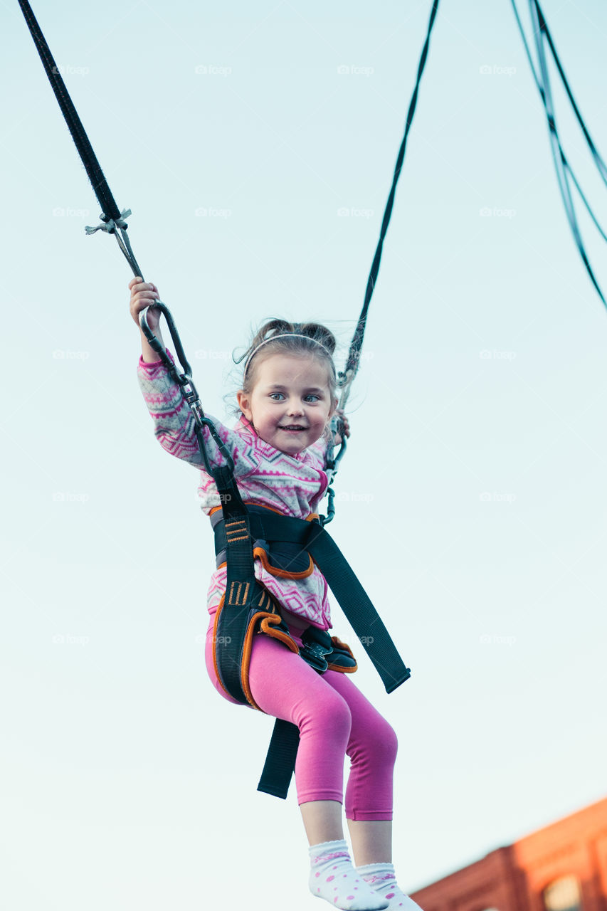 Little adorable smiling girl jumping on trampoline, having fun at funfair