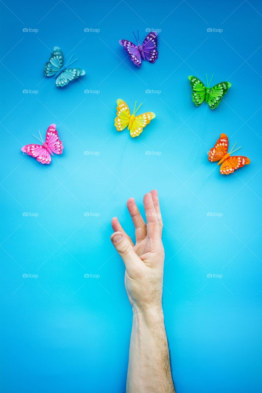 A hand reaching for a group of butterflies with a blue background.