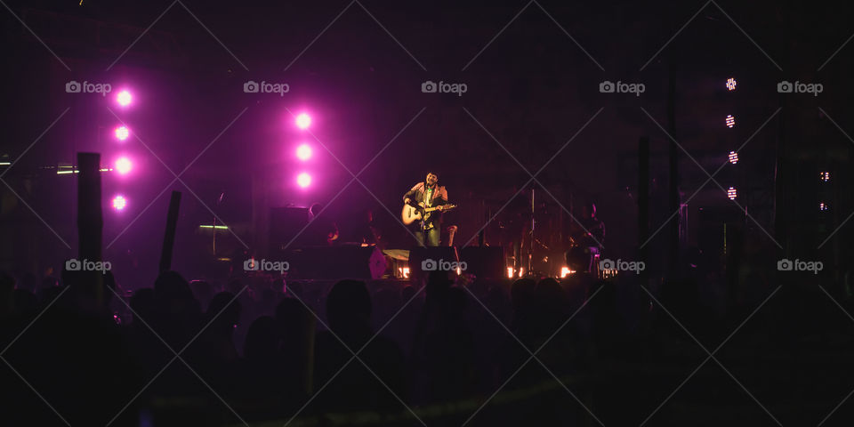 Kolkata India 1 May 2019: Guitarist performing on. Rock Concert venue with lit bright colorful stage lights and silhouette of fans or cheering crowd in front of it. Summer music background concept