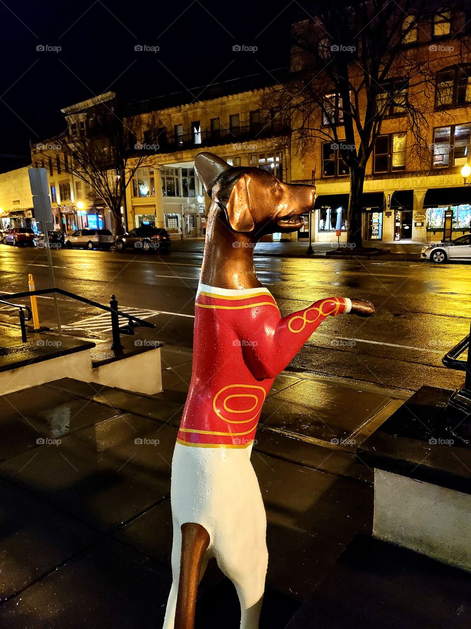 A dog in a fancy outfit greets visitors to a business on a downtown city street