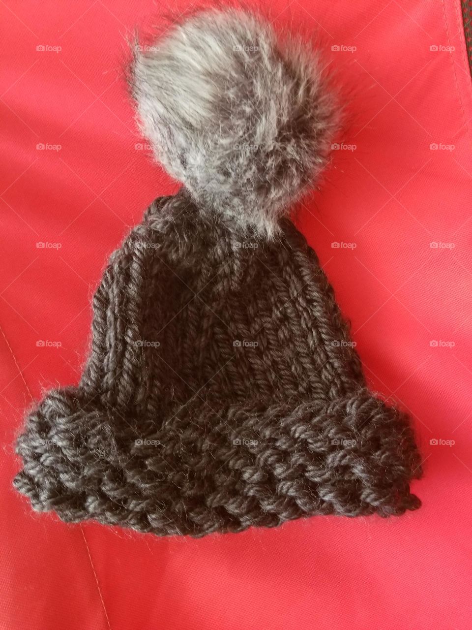 Knitted charcoal grey winter hat with pompom, on red background.