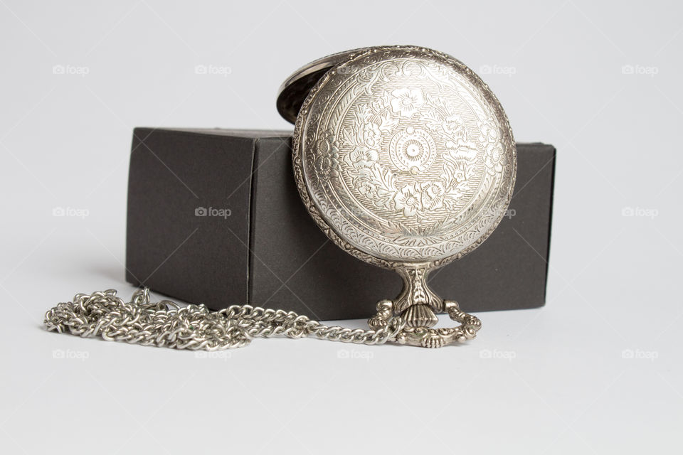Isolated miniature silver pocket watch with flower patterns and a black box macro shot
