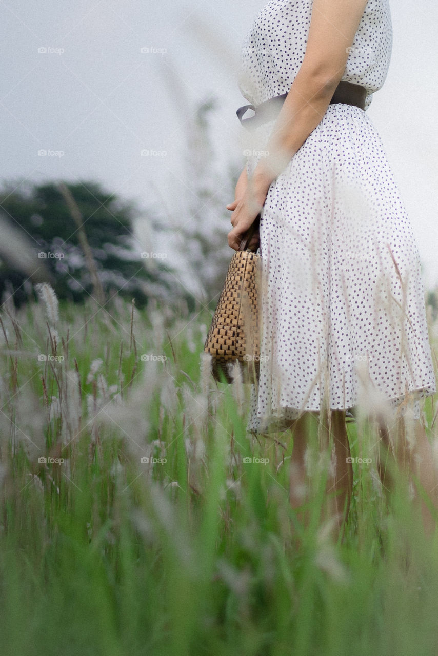 A half view of a woman standing holding a bag in the middle of a greeny grass, a day at outdoor