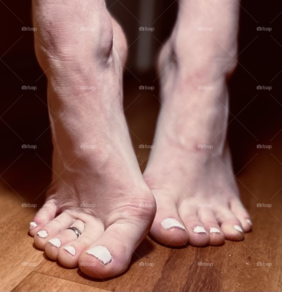 Strong Dancer Feet standing on hard wood floor on tippy toes showing off bunions with veiny wide feet and white pedicure