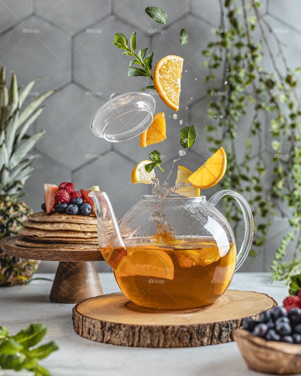 Tea pot with flying ingredients lemon, mint and orange slices 