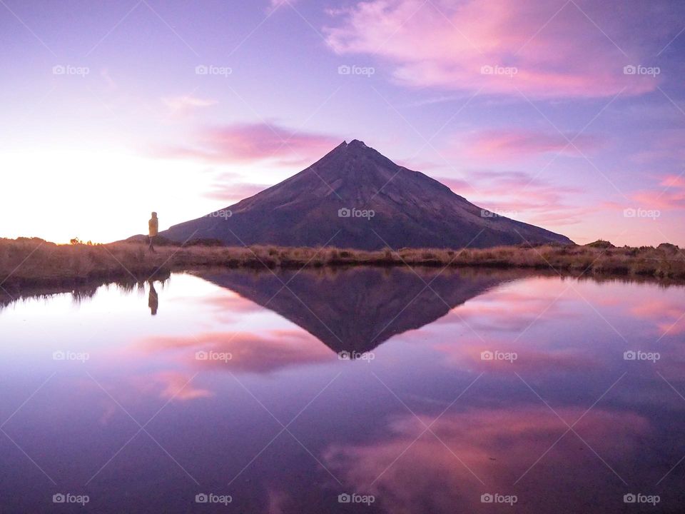 The sun rising over the mountain casts a beautiful pink and lilac light over the sky and casting a perfect reflection onto the lake
