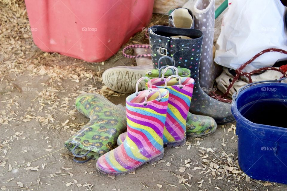 A collection of colorful children’s muck / mud boots on the floor of an open air barn 