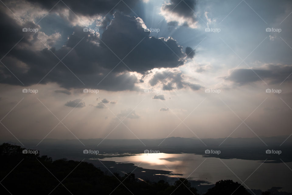 Sun shining through clouds over lake at dusk