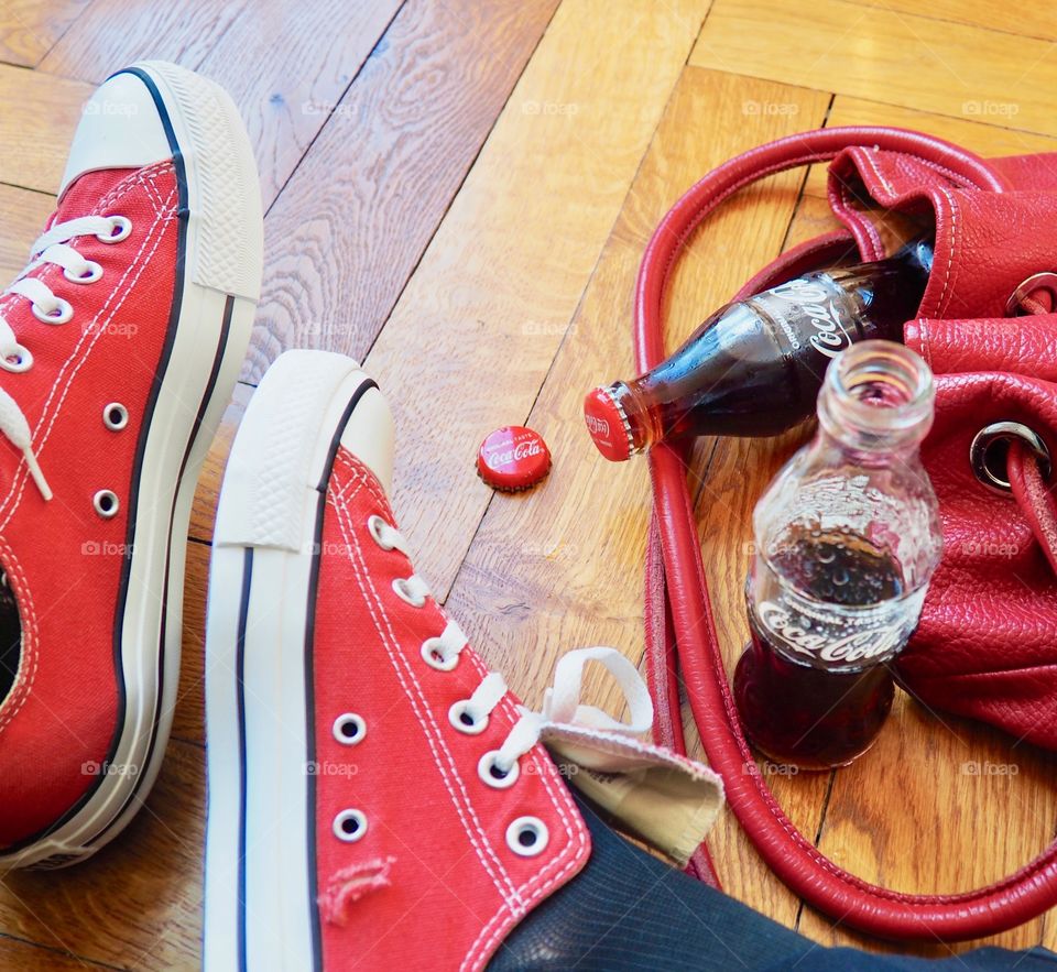 Coca Cola bottles on hardwood floor with red sneakers and red leather bag.