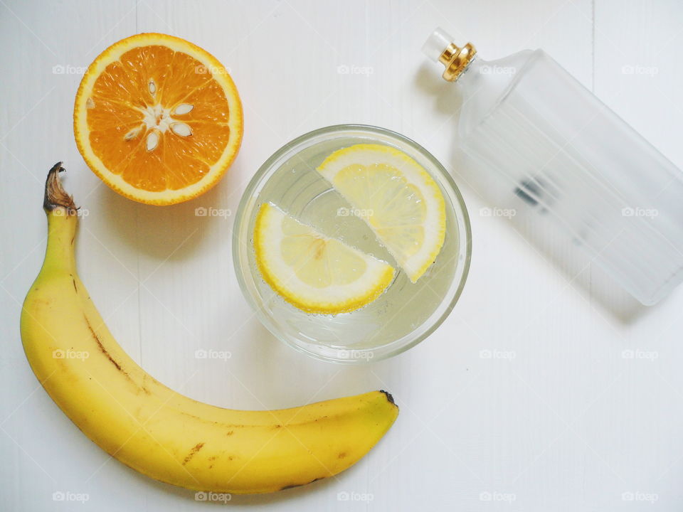 lemonade with lemon, orange, banana and eau de toilette on white background