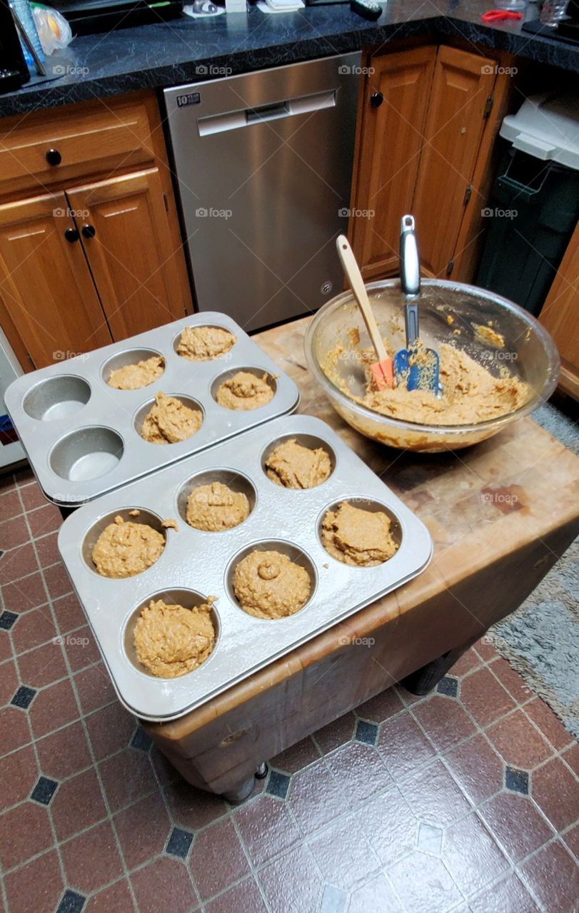 Filling & baking muffins using two muffin tins. Glass bowl holds homemade mixture and utensils.