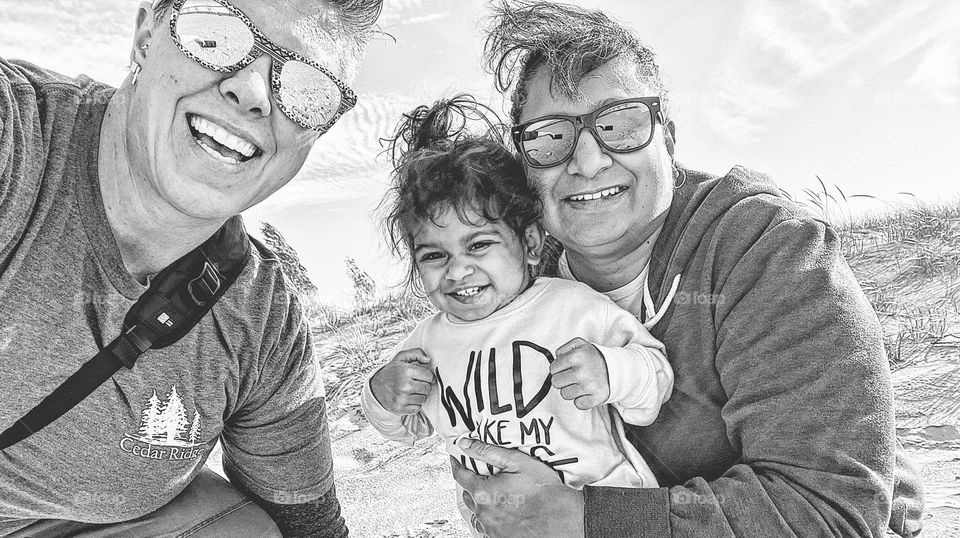 Black and white photo of family smiling, happiness is being together, happy family portrait, family is happy together, family on the beach together, happiness in a portrait, facial expressions portraying happiness, LGBTQ family smiling on a beach 