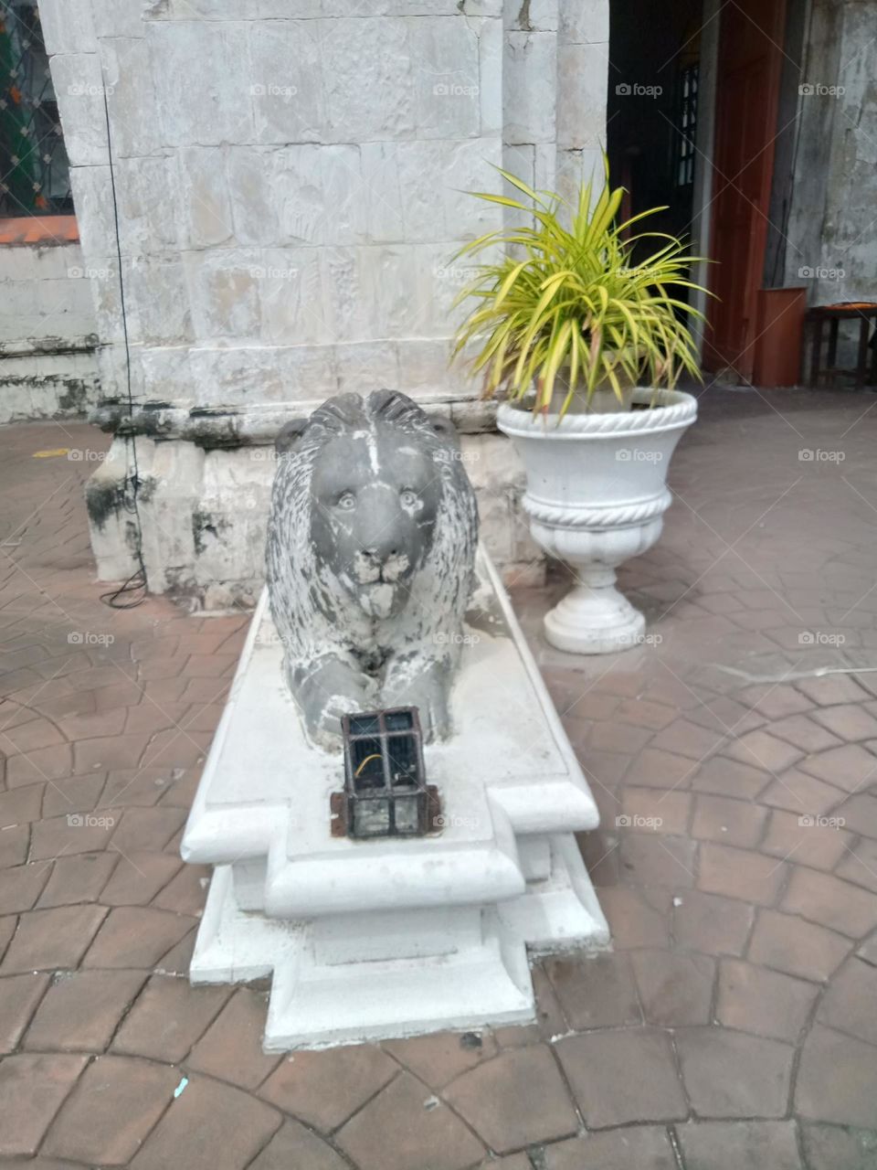 A SCULPTURE OF A WHITE LION IN FRONT OF A BUILDING WITH SIDE PLANT