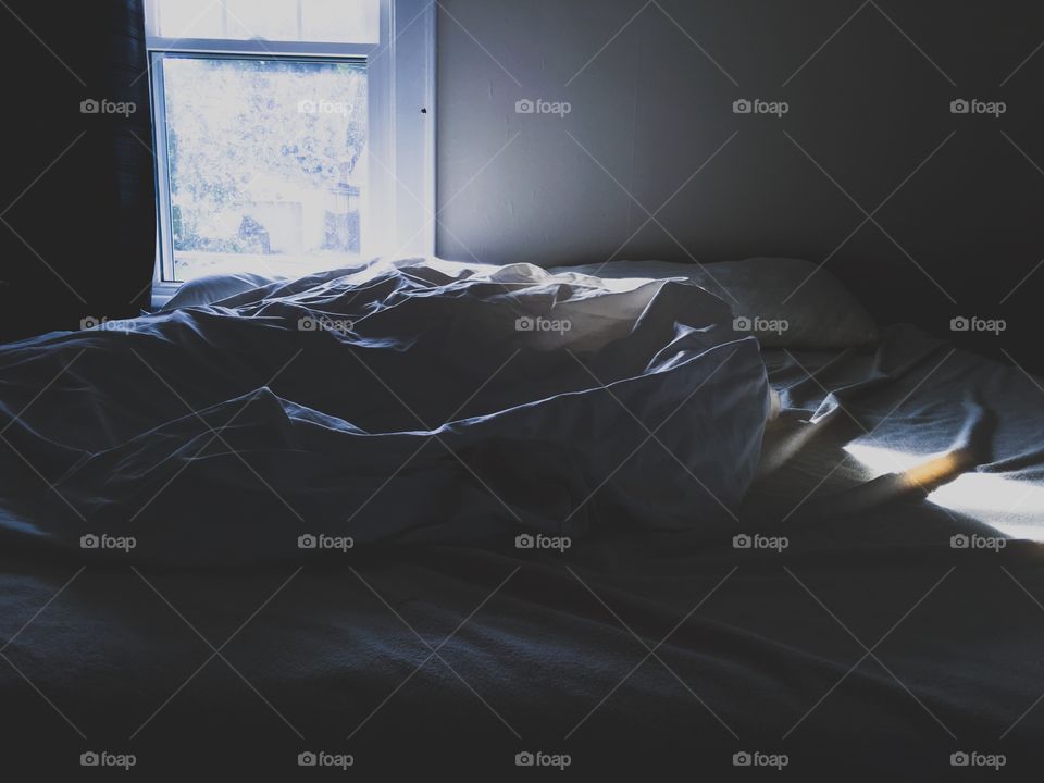 White sheets on a bed next to a window with early morning sunshine starting to show in the bedroom 