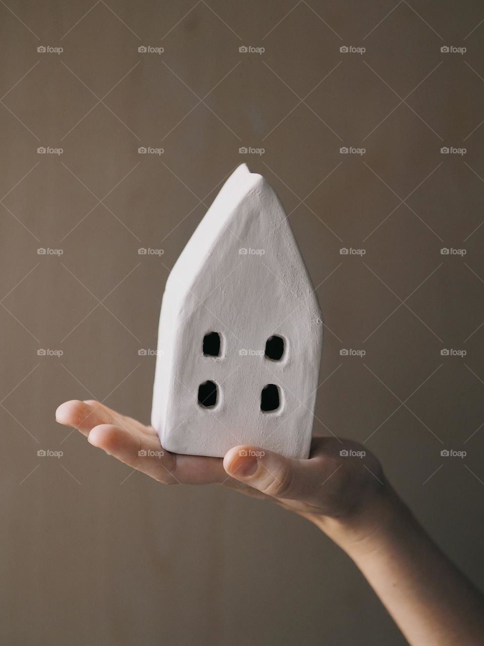 Young unknown girl's hand holds a triangular ceramic house on a beige background