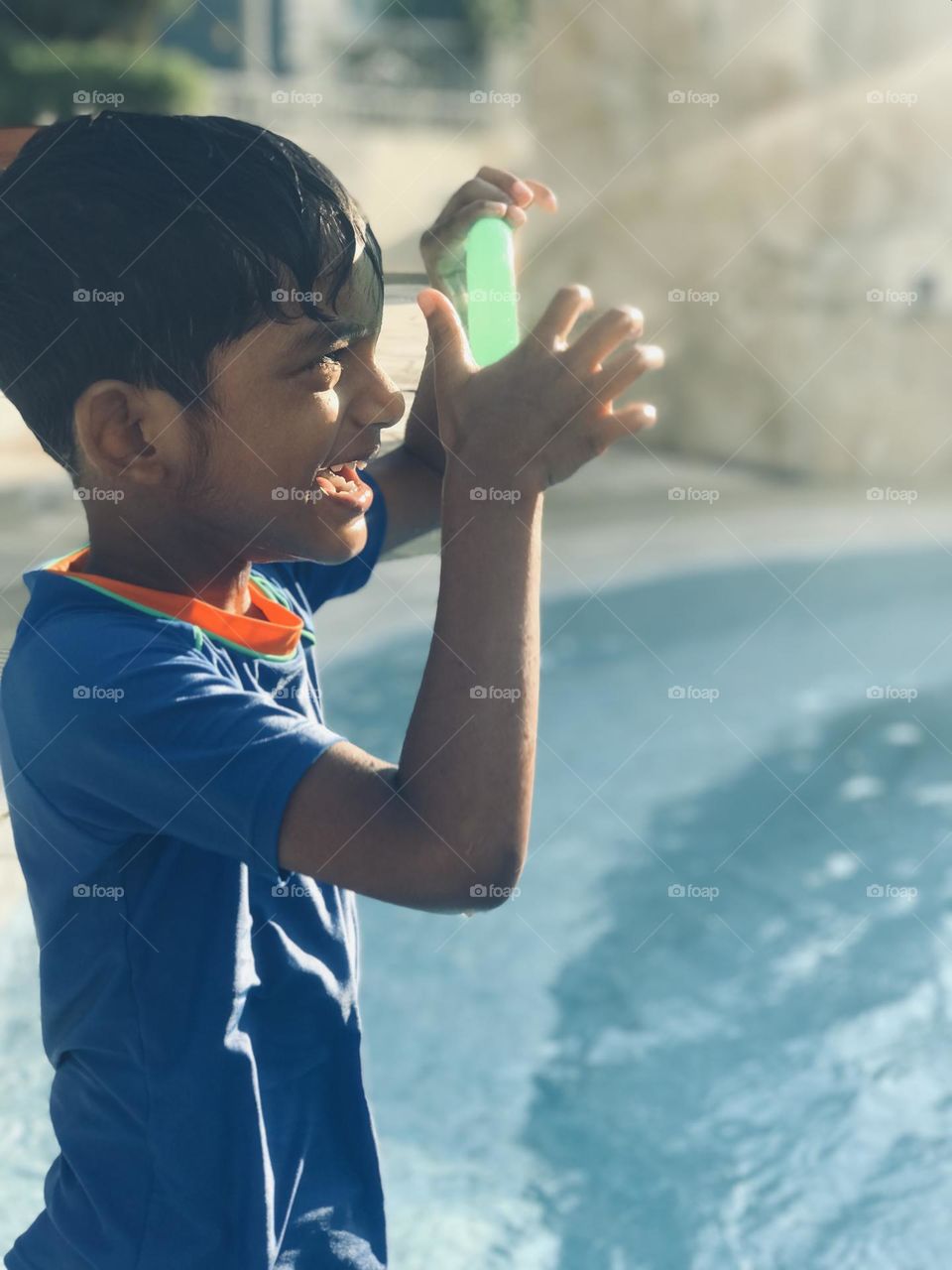 A boy looking towards sun through the green colour circle and making funny moments at swimming pool in summer time.