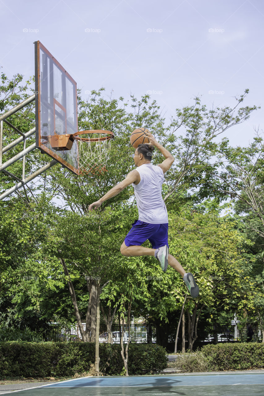 Basketball in hand man jumping Throw a basketball hoop Background  tree in park.