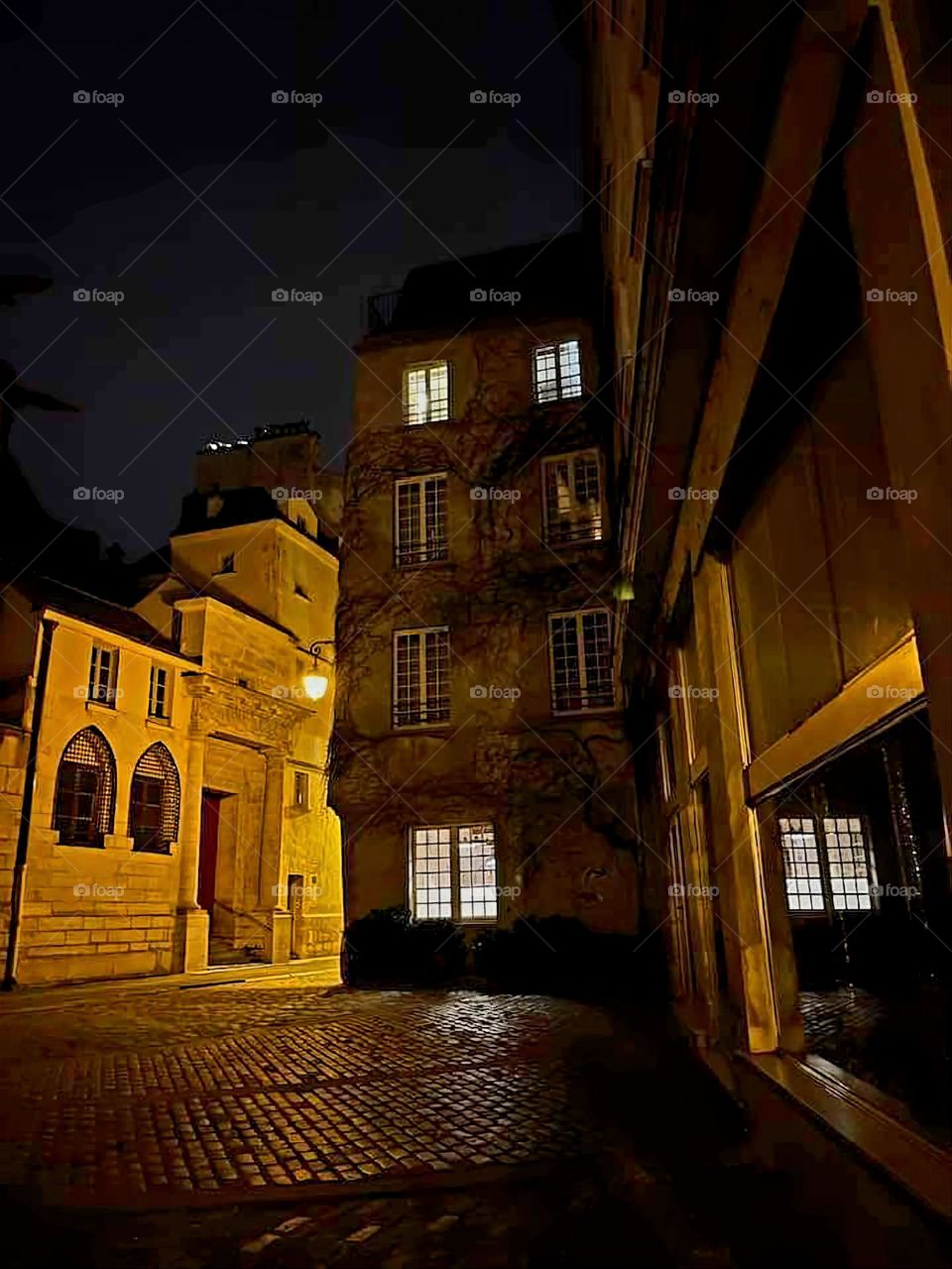 Illuminated small-paned windows of the facade of a parisian building at nightfall in Paris, in des Barres street, under a dark sky