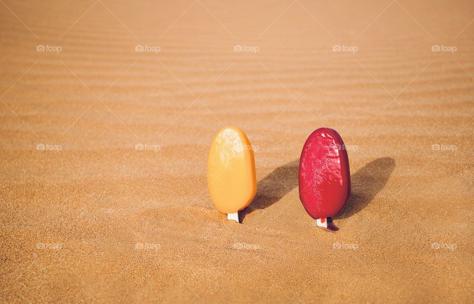 Colorful ice cream melting in hot desert sand 