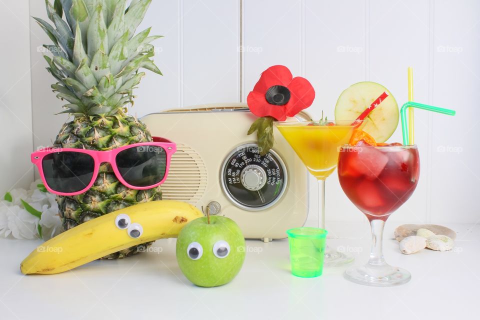 Fruit with funny eyes and glasses next to cocktails and a vintage radio