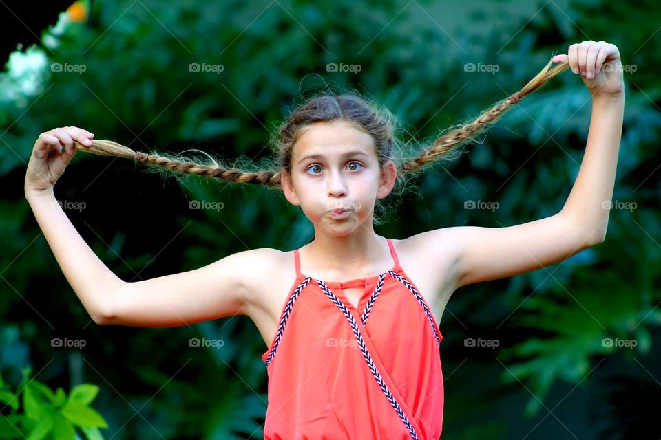 cute young girl making a funny face with crossed eyes and puffy cheeks while pulling on her braided pig tails