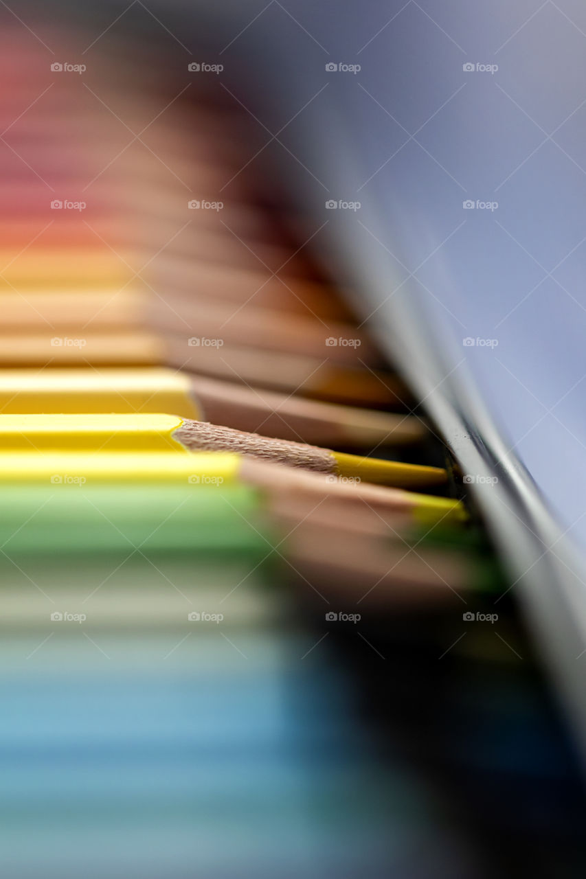 an isolated close up of a yellow colored pencil lying between other colored pencils inside a box, making a colorful picture.