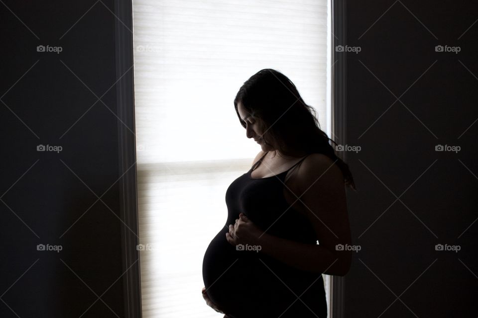 Pregnant woman touching her belly in dark room