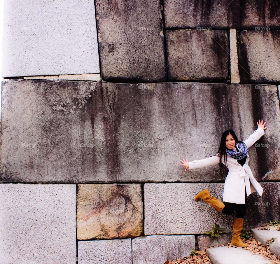 Asian woman posing in front of big stone wall