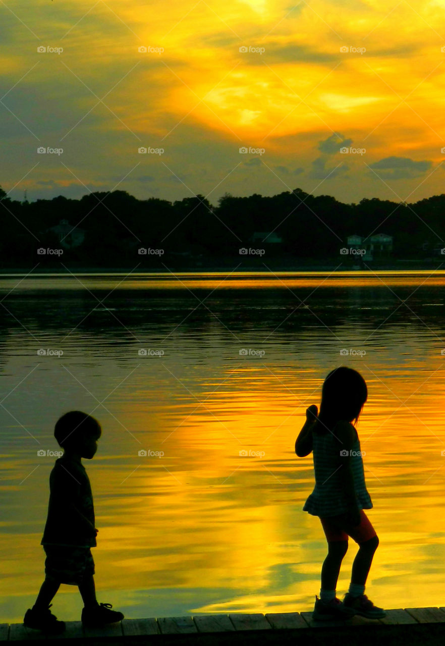 A brother and sister walk the plank at the park in front of a magnificent sunset!