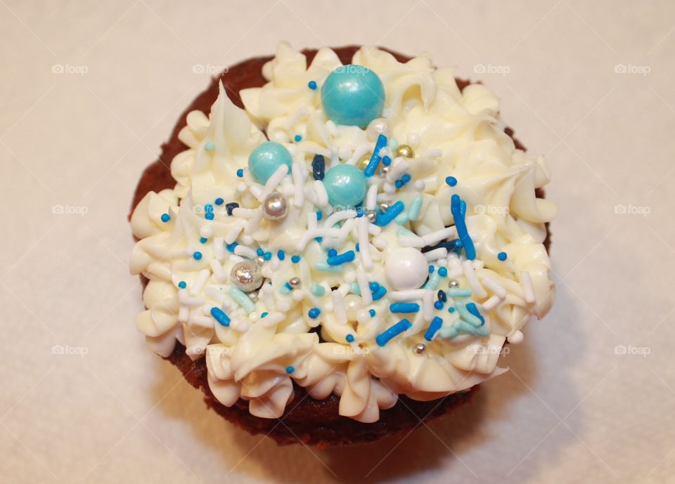 Christmas baking time! Closeup of a red velvet cupcake with vanila icing and blue, white, gold and silver sprinkles and dragees. Yummy!