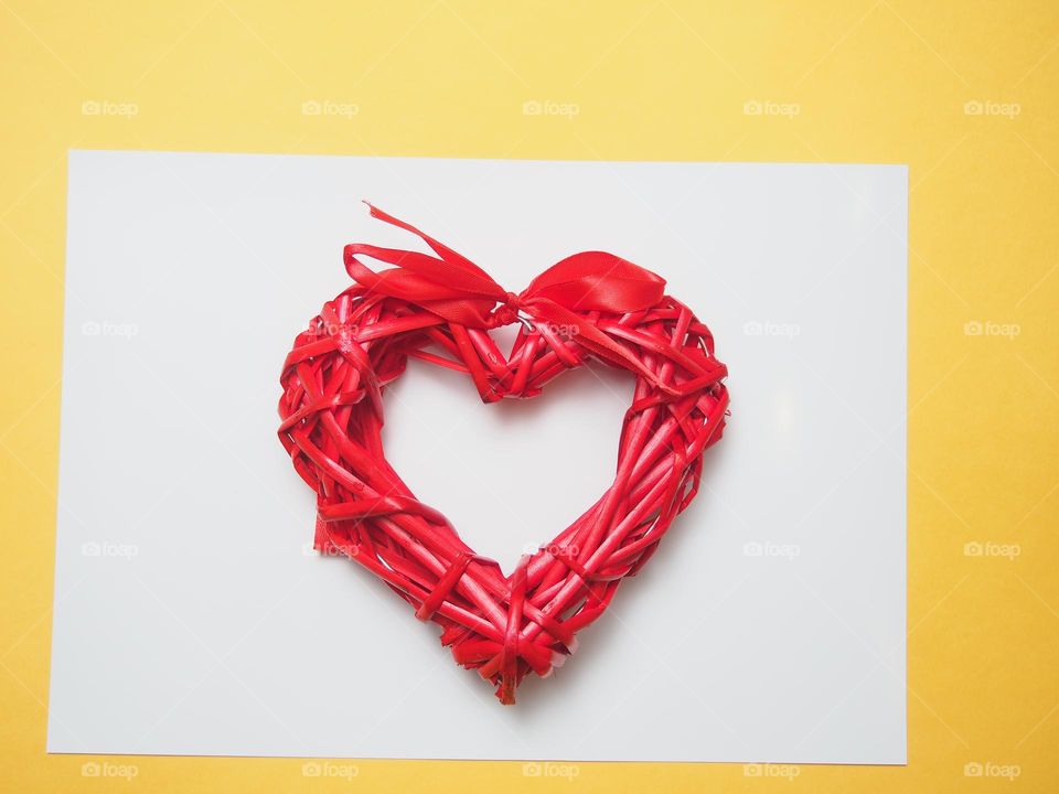 A heart woven from red sticks lies on white paper.