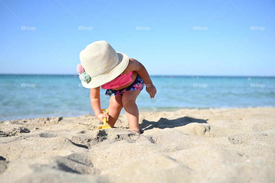 little girl with straw hat playing on the beach