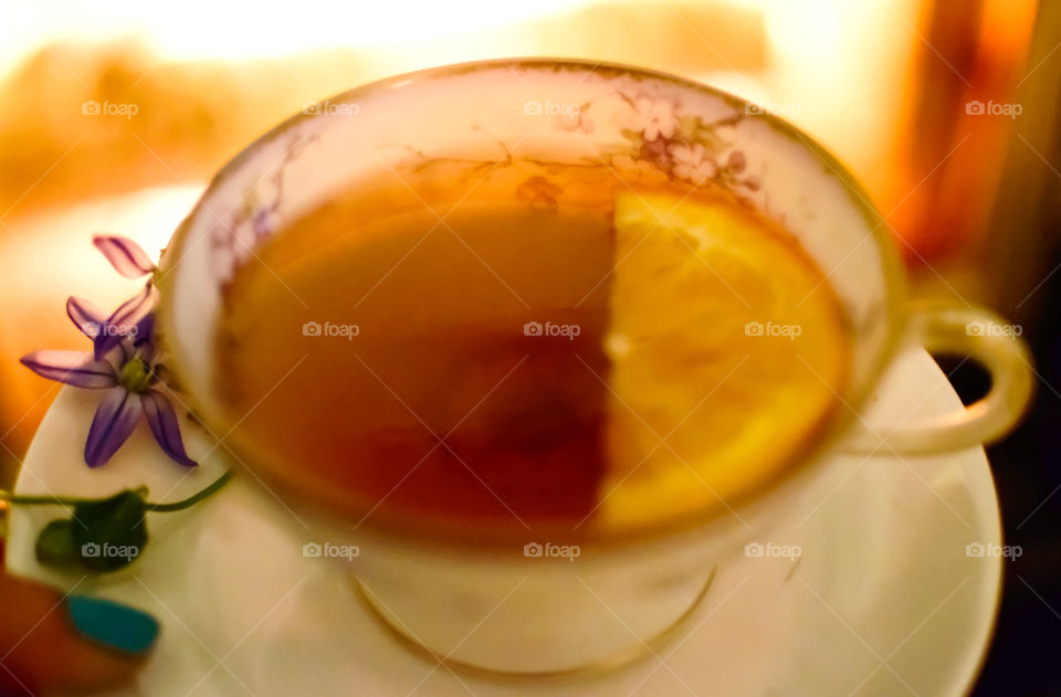 Holding a cup of tea by the fire in vintage tea cup with orange slice fruit and fresh garden flowers 