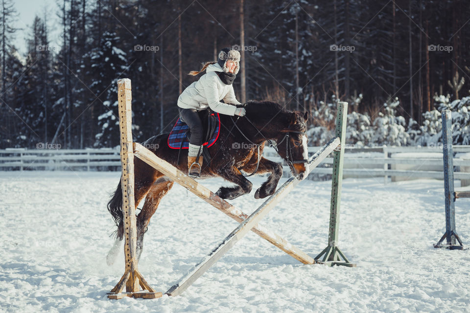 Teenage girl horseback jumping at cold winter day 