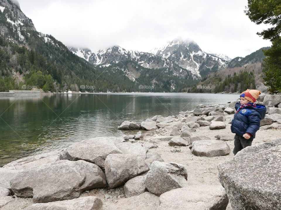 Little boy standing near lake and mountain