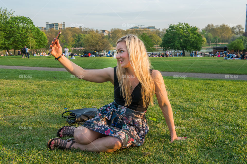 Woman sitting on grass taking selfie on mobile phone