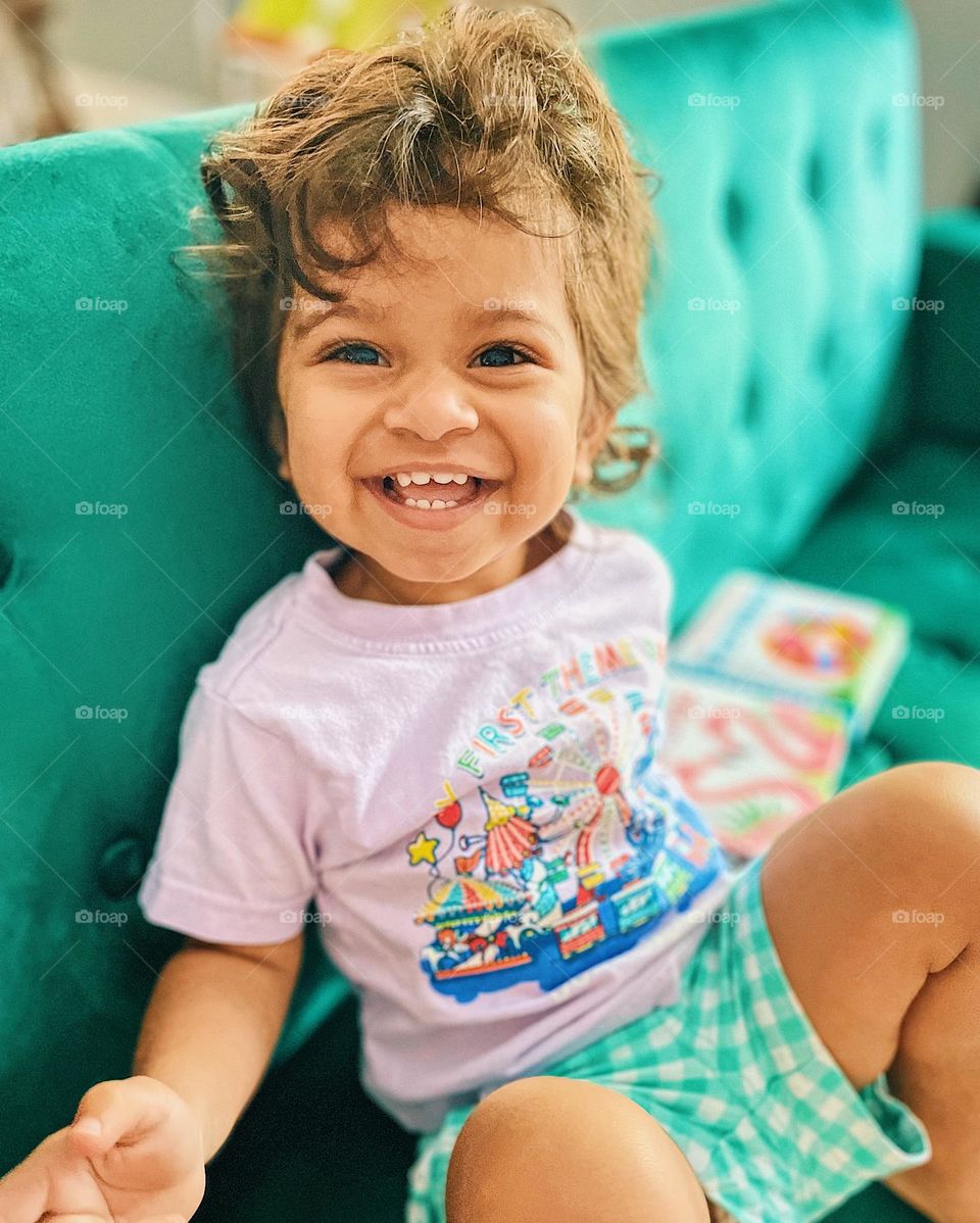 Happy toddler smiling at the camera, happiness on a toddler’s face, toddler shows the emotion of happiness, toddler is happy on the couch, cute toddler smiling, toddler is happy and smiling, happiness is a big smile, smiling ear to ear, joyful baby