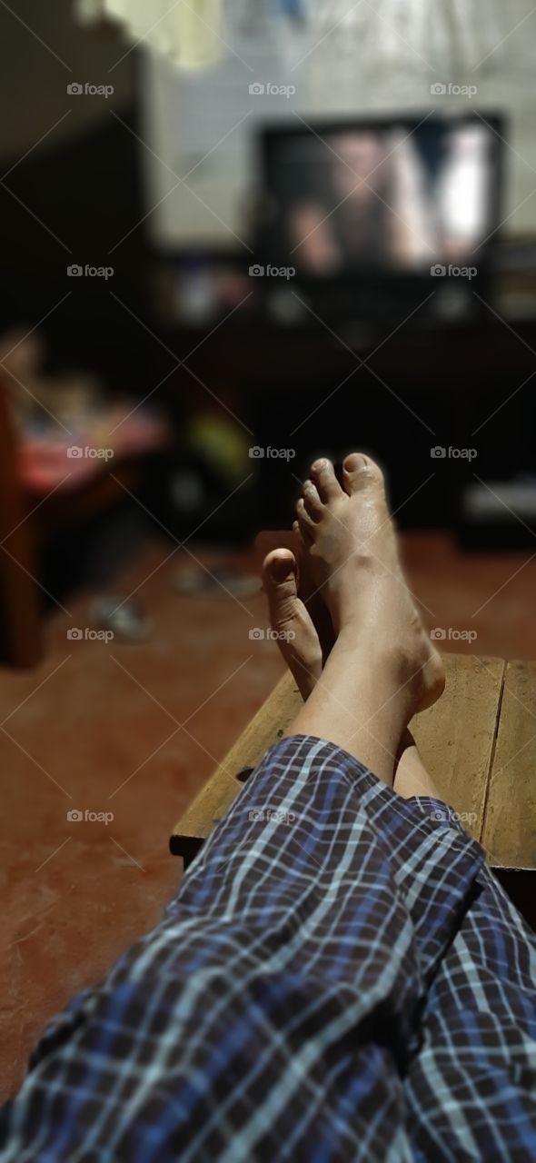 watching tv in relax way...feet raised on stool and tv in the blur background