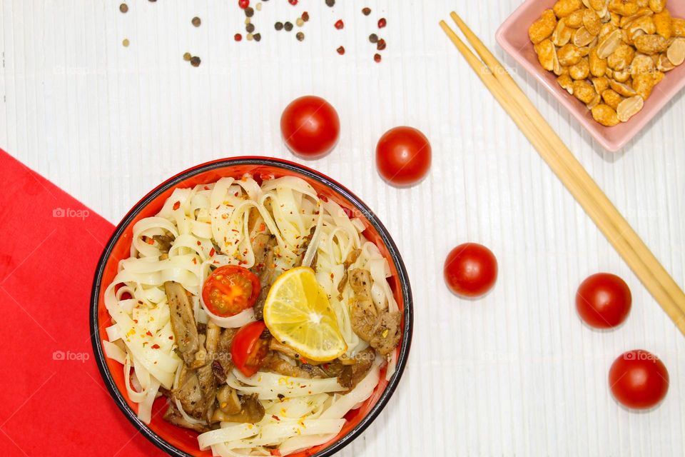 Rice  noodles with oyster mushrooms in a red bowl on a wooden background